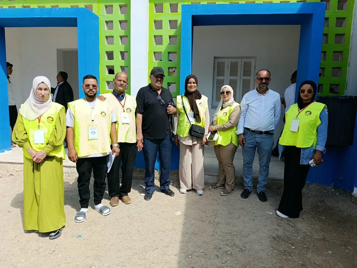 مجموعة من المتطوعين والإطار الصحي بسترات صفراء وخضراء واقفون في صورة جماعية أمام مدخل ملوّن
