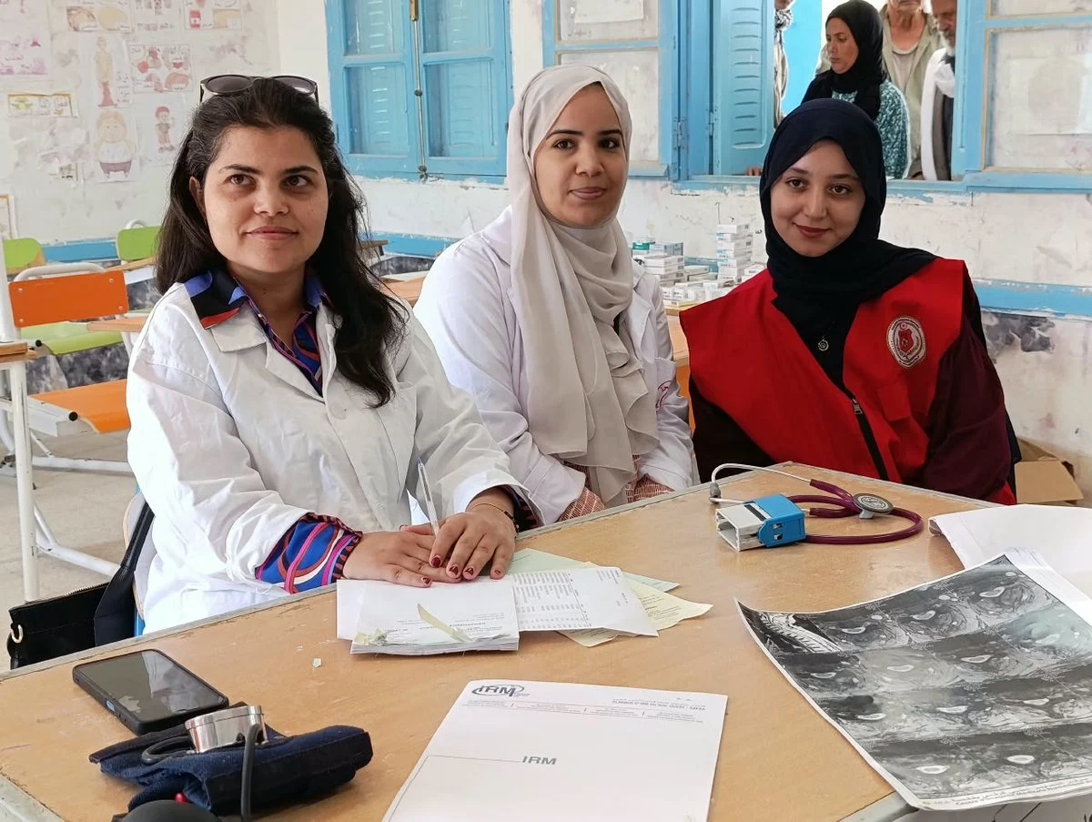 ثلاثة من الإطار الصحي والمتطوعين خلف طاولة عليها جهاز قياس الضغط وصور أشعة