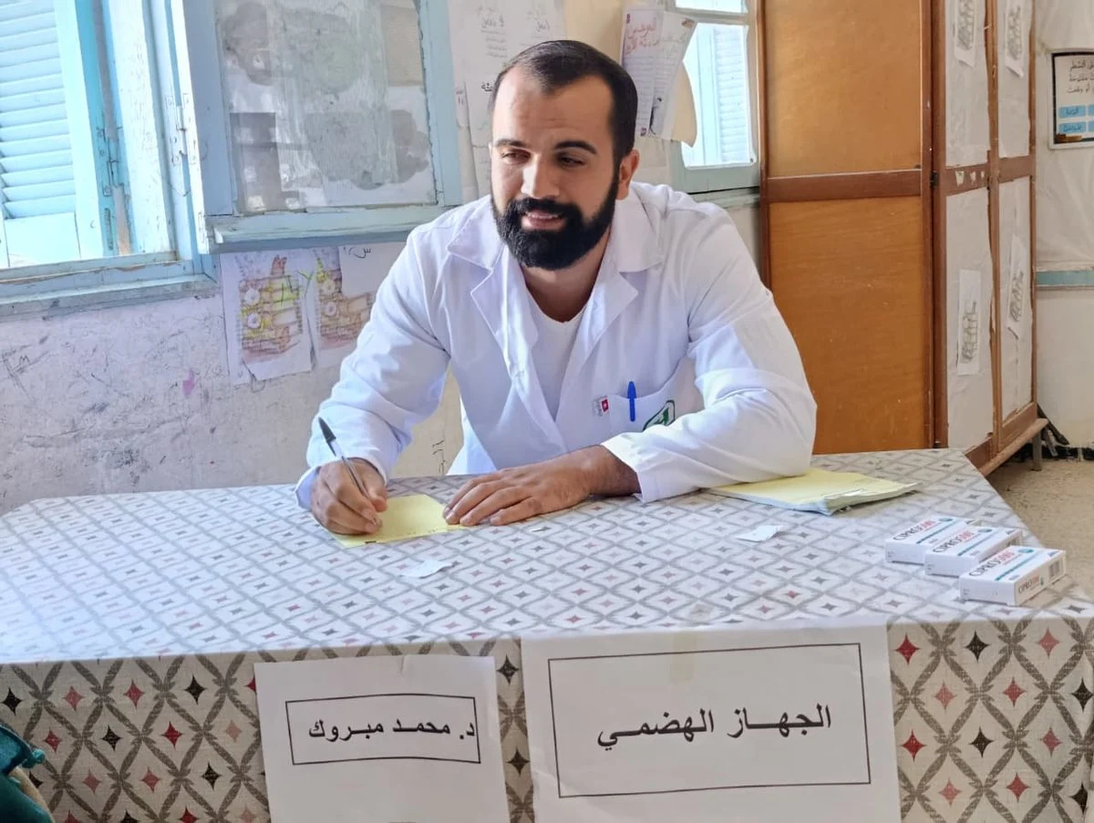 طبيب بمئزر أبيض يكتب على الطاولة أمام لافتة «الجهاز الهضمي»