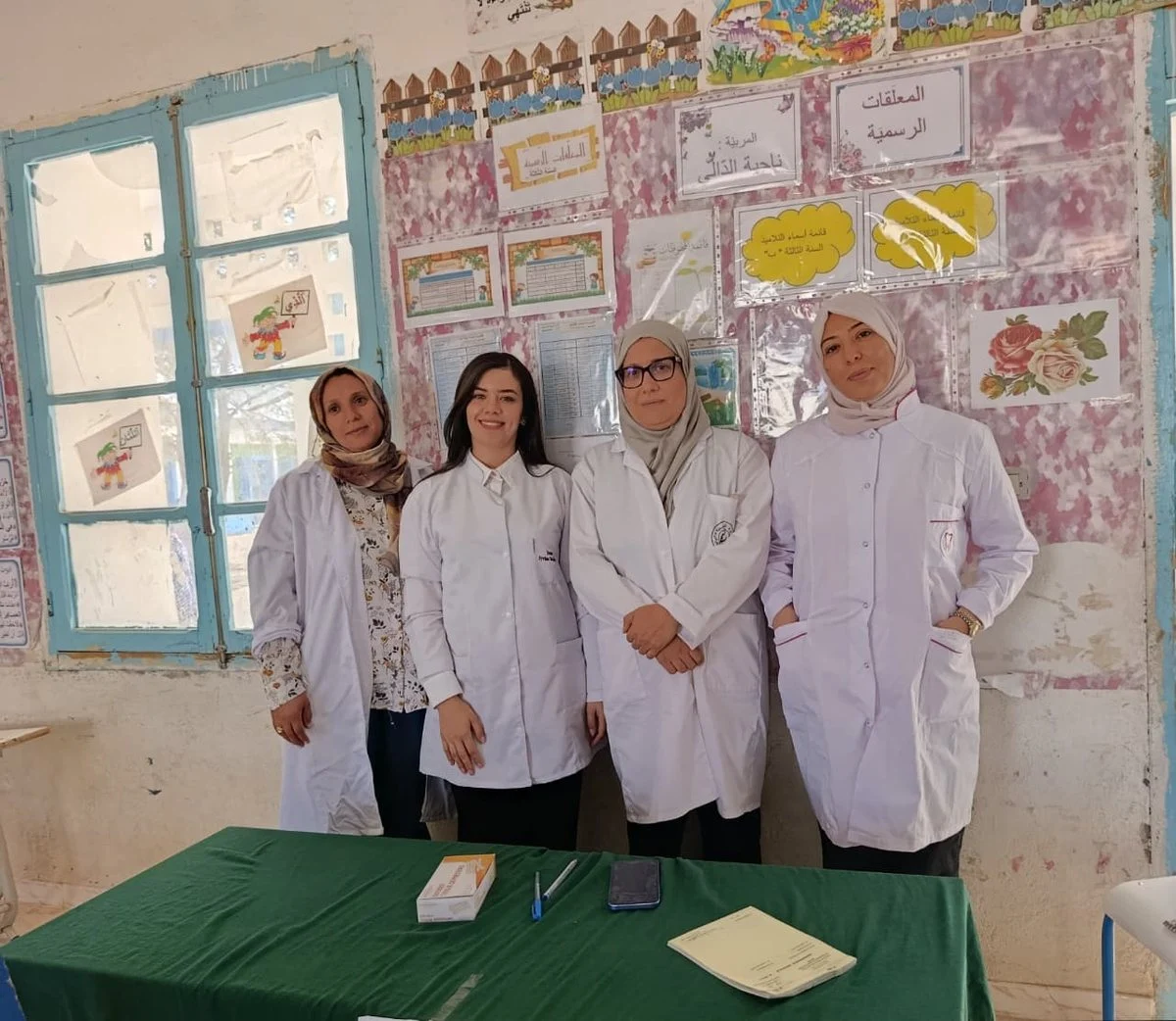 أربع طبيبات بمآزر بيضاء واقفات في صف واحد خلف طاولة خضراء داخل قاعة