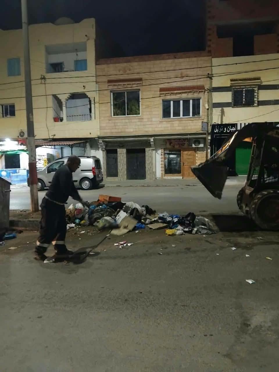 عون نظافة يكنس كومة فضلات على حافة الطريق ليلا أمام مبان سكنية في قفصة