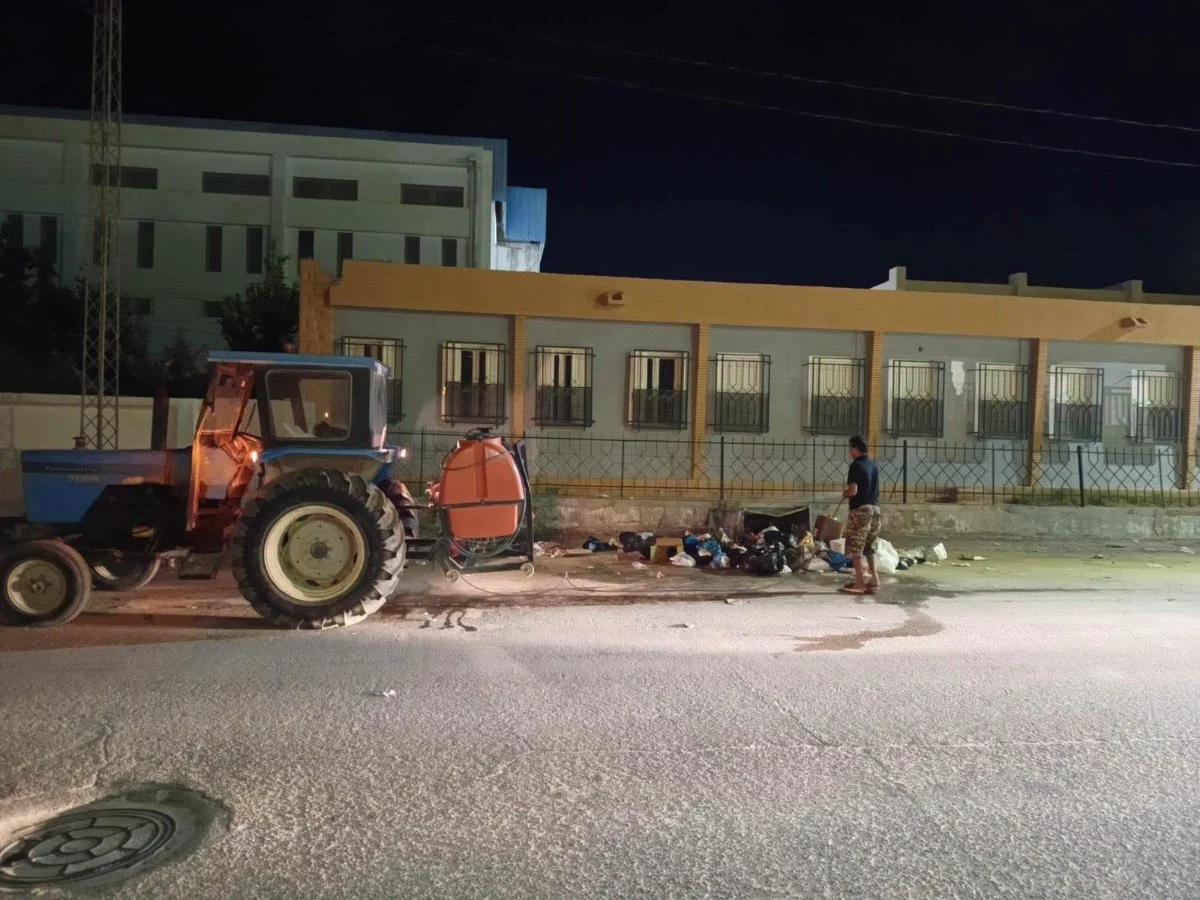 عامل من فريق المداواة ببلدية قفصة يرش محيط كومة فضلات أمام سور مبنى ليلا وإلى جانبه جرار يجرّ خزانا برتقاليا