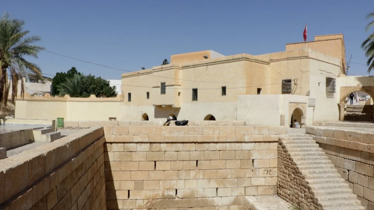جدران الأحواض الرومانية بقفصة من الحجر المنحوت ودرج حجري، وخلفها مبانٍ بيضاء في المدينة العتيقة