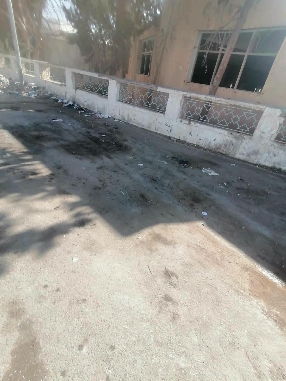 فضلات وبقع داكنة على الإسفلت أمام سور مبنى مهجور بنوافذ مكسورة بقفصة