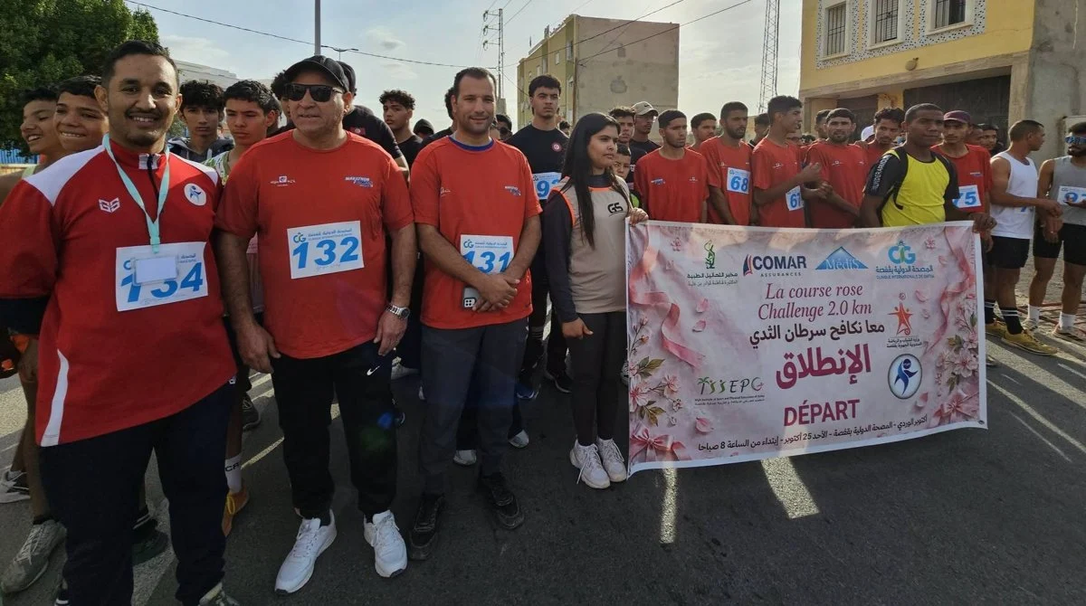 مشاركون يحملون أرقام السباق يقفون إلى جانب لافتة «معا نكافح سرطان الثدي» عند خط الانطلاق