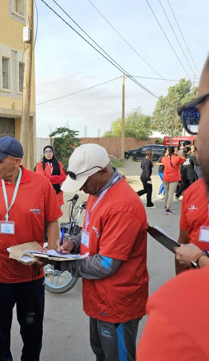 عضوان من فريق التنظيم بقمصان حمراء يدوّنان أسماء المشاركين على لوح كتابة