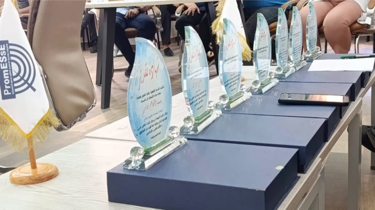 مجسمات شهادات تقدير زجاجية مصفوفة على علب زرقاء فوق طاولة خلال حفل التكريم