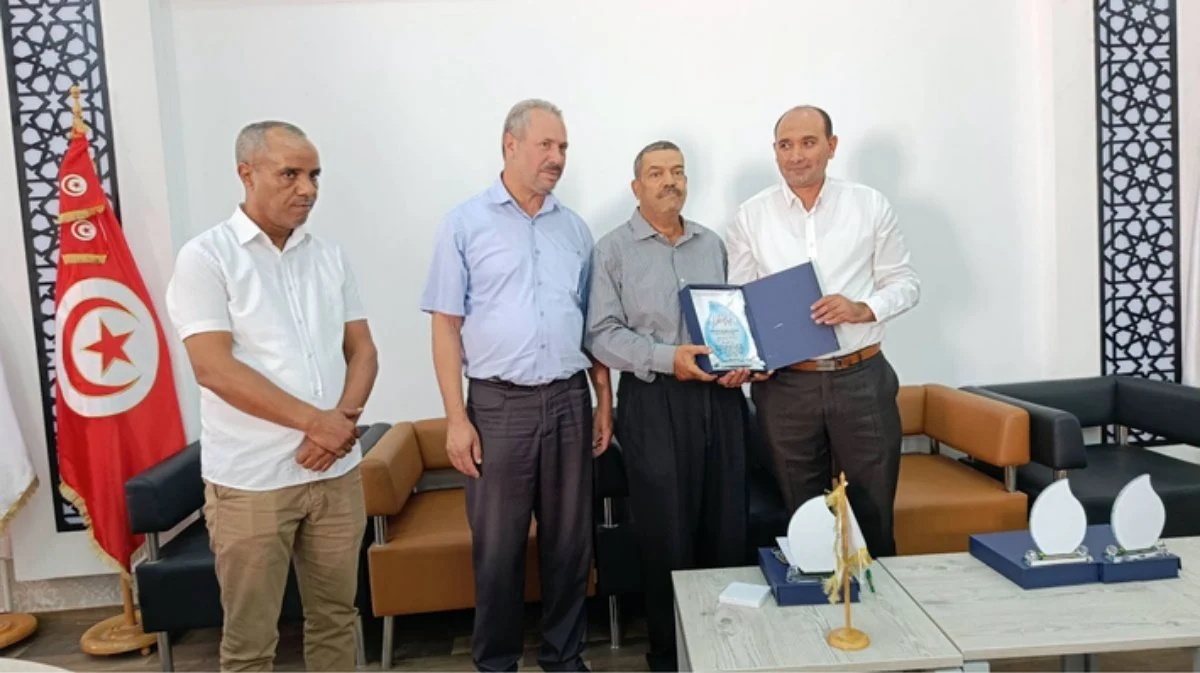 أربعة رجال يتسلّم أحدهم شهادة تقدير أمام العلم التونسي في قاعة الحفل