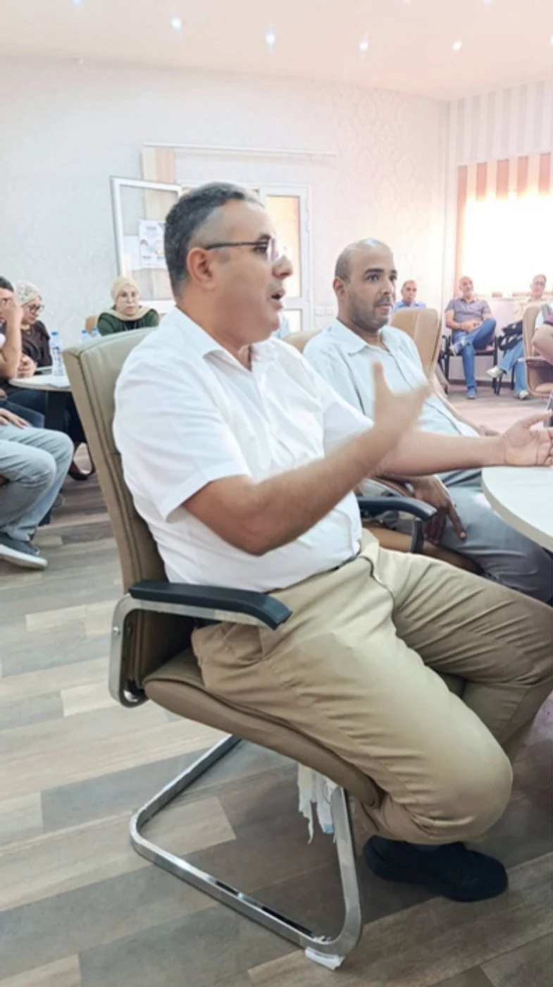 أستاذ بقميص أبيض يتحدث جالسا خلال الحفل وإلى جانبه أحد الحاضرين