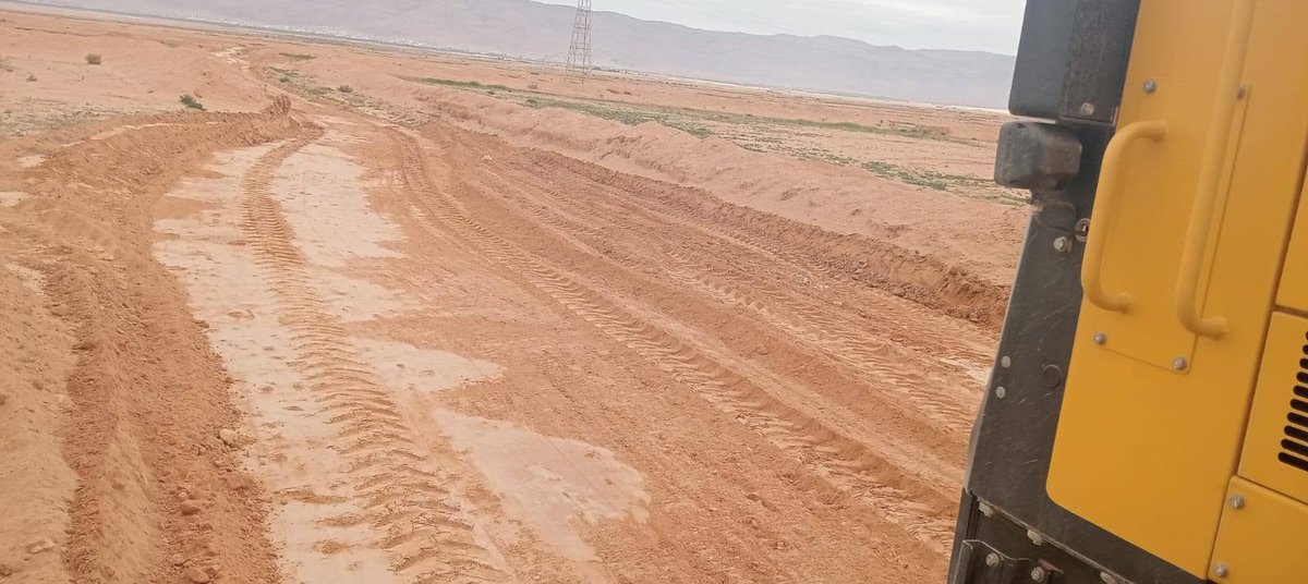 مسلك ترابي أحمر بعد مسحه تظهر فيه بقايا مياه الأمطار وجبال في الأفق
