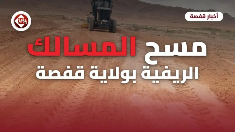 آلة تسوية تعمل على مسلك ترابي أحمر في سهل تحيط به الجبال، مع عنوان «مسح المسالك الريفية بولاية قفصة» وشعار راديو كابصا اف ام