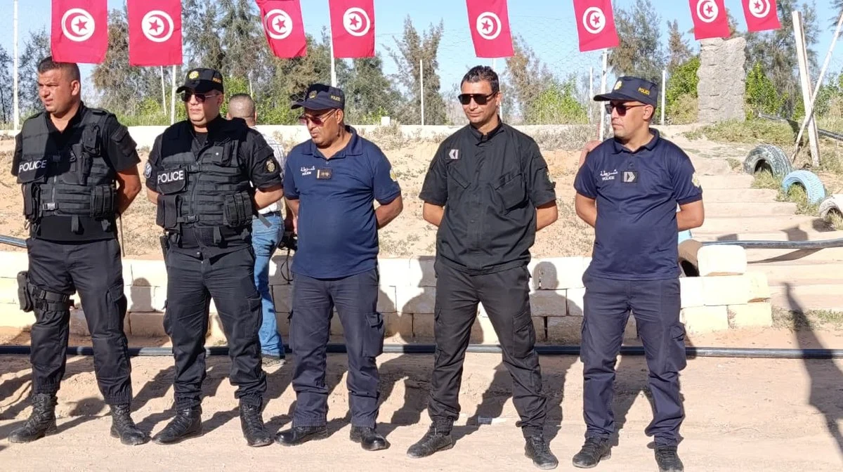 خمسة أعوان من الشرطة الوطنية يقفون في صف تحت أعلام تونسية معلّقة بساحة جمعية التفاؤل بقفصة