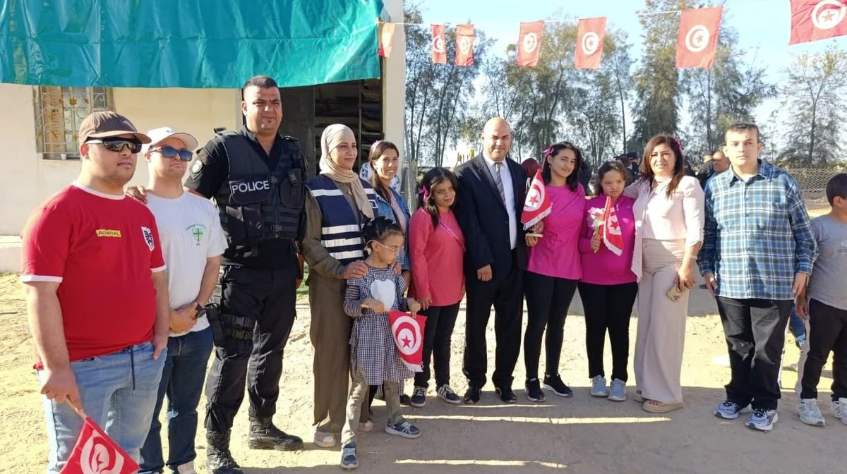 مجموعة من أطفال وشباب جمعية التفاؤل مع عون أمن وضيوف يحملون أعلاما صغيرة تحت أعلام معلّقة بقفصة