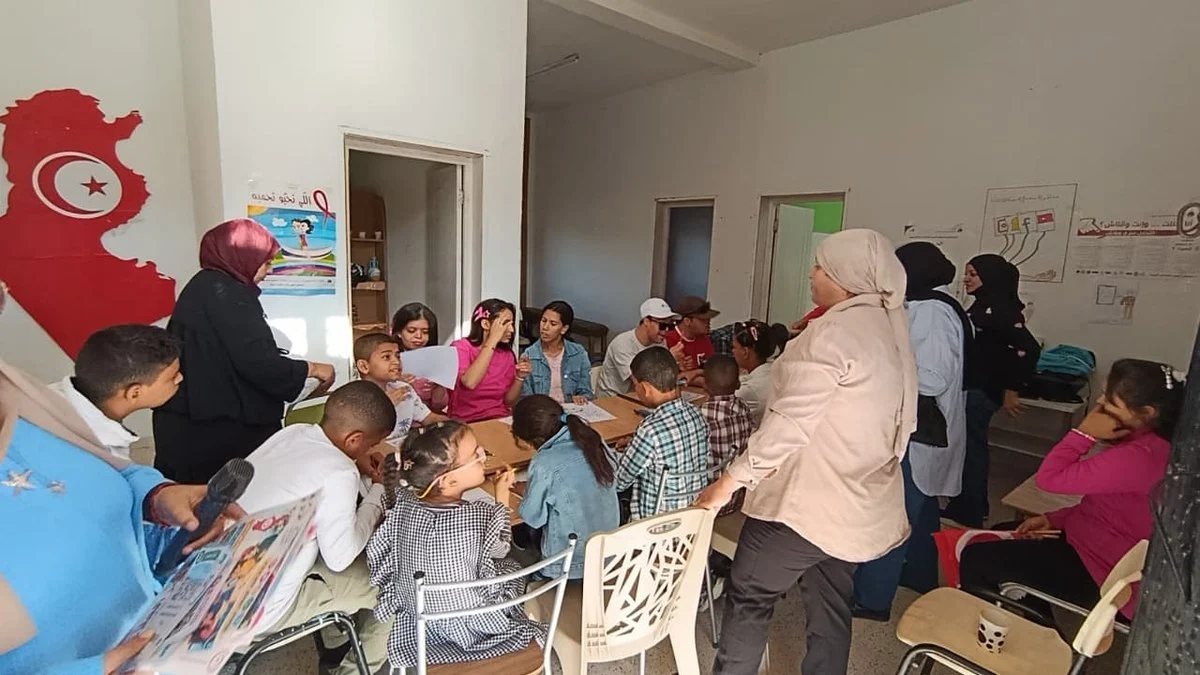 أطفال يرسمون حول طاولة في قاعة جمعية التفاؤل بقفصة تحت خريطة تونس المرسومة على الجدار