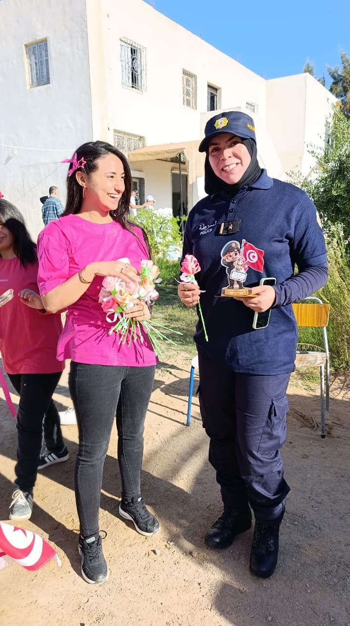 عونة أمن مبتسمة تحمل وردة ومجسّما صغيرا للعلم التونسي إلى جانب شابة من جمعية التفاؤل بقفصة