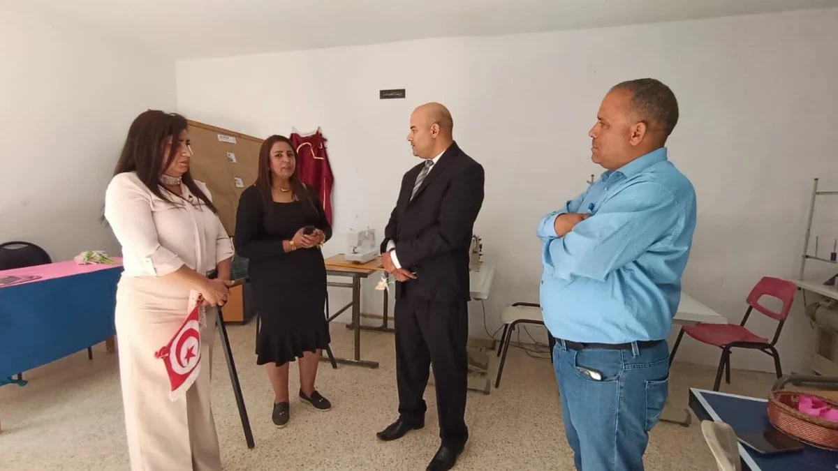 ضيوف يزورون ورشة الخياطة بجمعية التفاؤل بقفصة وبينهم رجل ببدلة سوداء وامرأة تحمل علما صغيرا