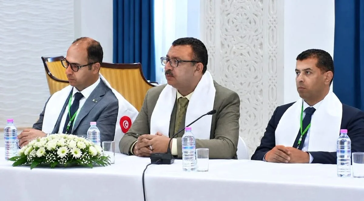 ثلاثة مشاركين بأوشحة بيضاء يجلسون خلف طاولة بيضاء مزينة بالورود خلال أشغال الاجتماع