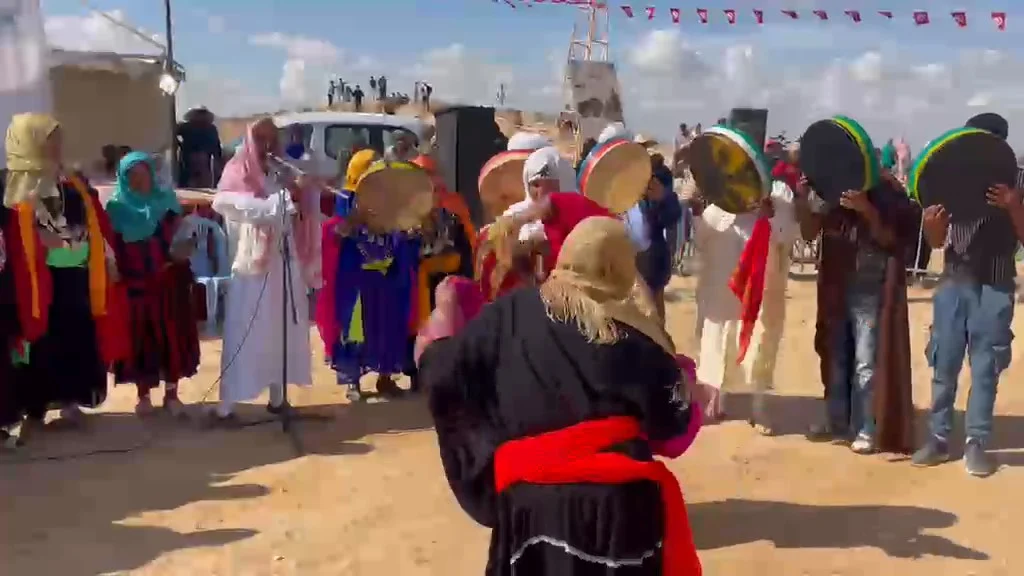 راقصة بلباس أسود وحزام أحمر تؤدّي رقصة الخطيفة أمام صفّ من عازفي البندير وعازف القصبة بأم العلق
