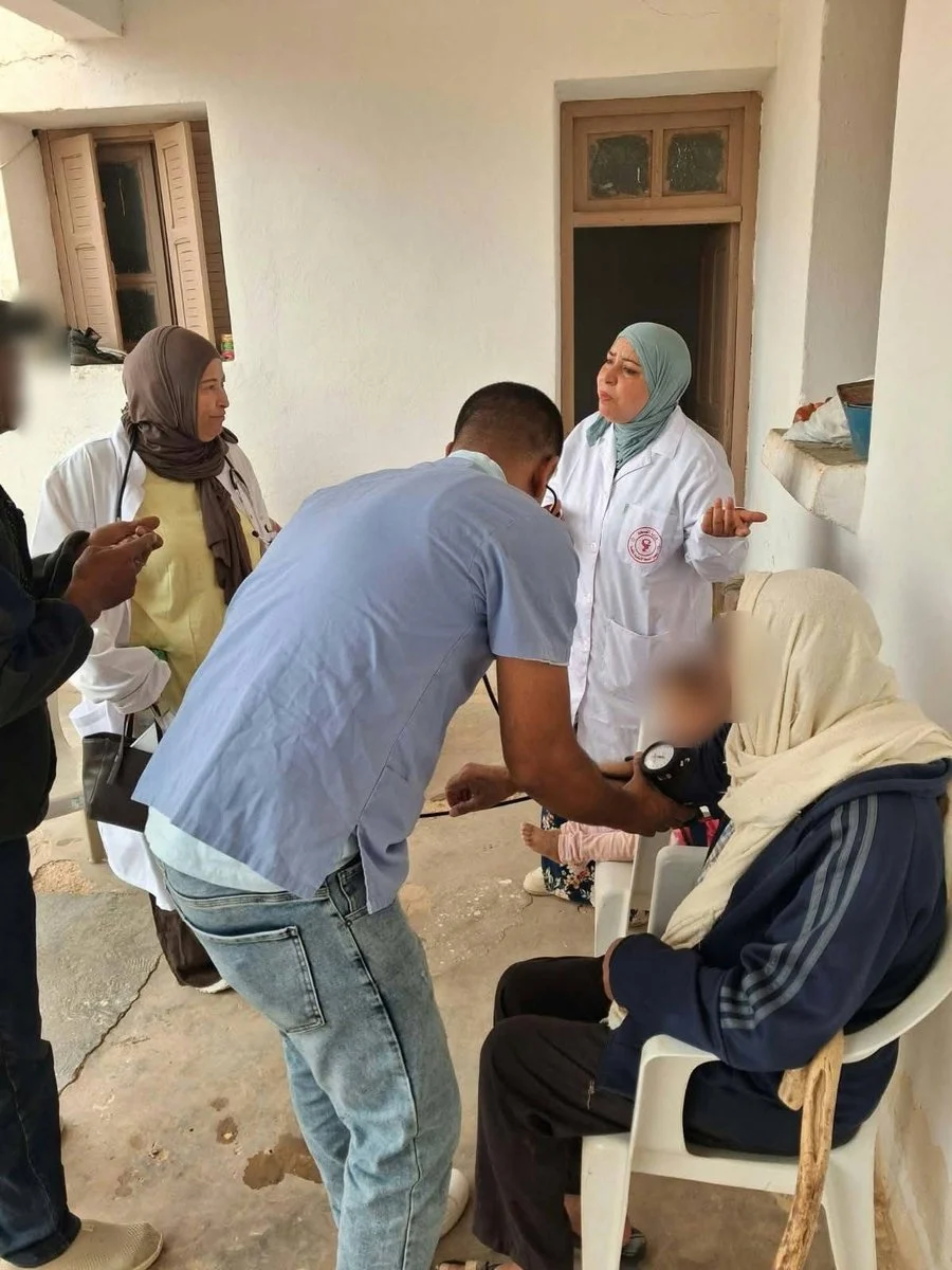 فريق صحي يقيس ضغط دم رجل مسنّ جالس أمام باب منزله في الوسط الريفي