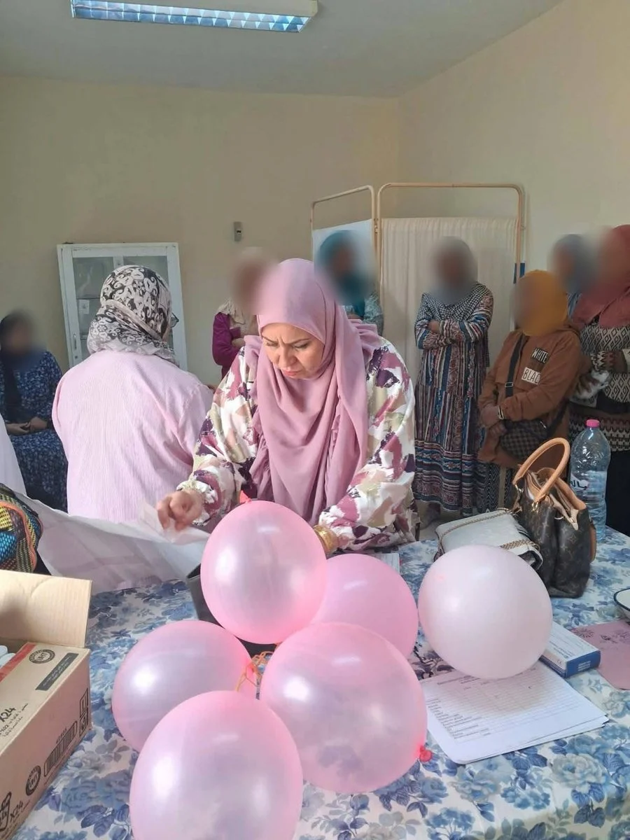 امرأة تحضّر بالونات وردية على طاولة أمام مجموعة من النساء خلال حصة توعية بالتقصي المبكر عن سرطان الثدي