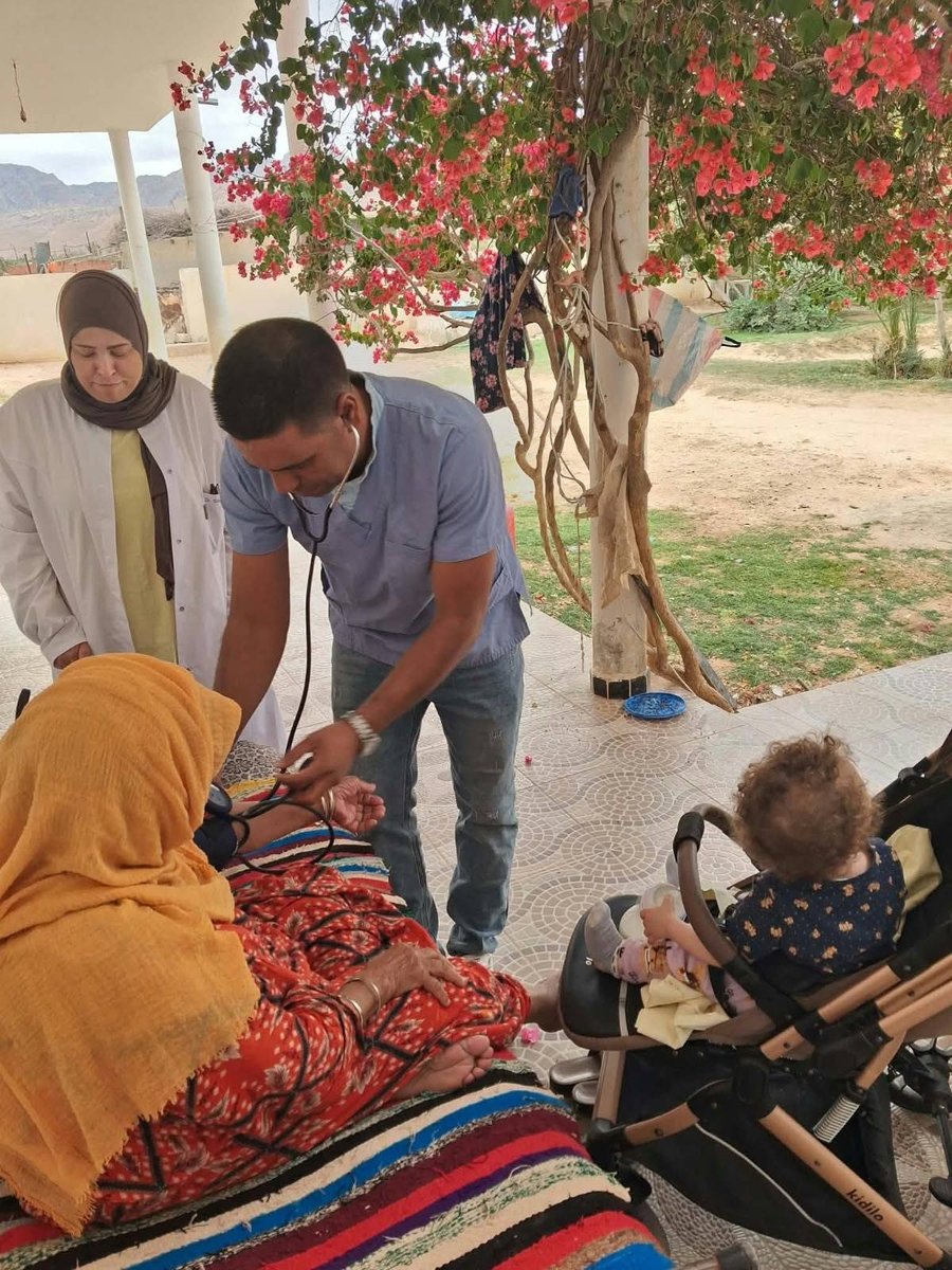 ممرض يقيس ضغط الدم لامرأة مسنّة تحت عريشة جهنمية مزهرة خلال زيارة منزلية بالوسط الريفي