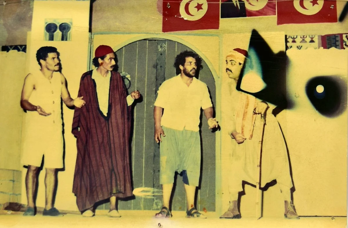 Photo en couleurs d'El Arich : quatre comédiens devant une porte bleue et des drapeaux tunisiens