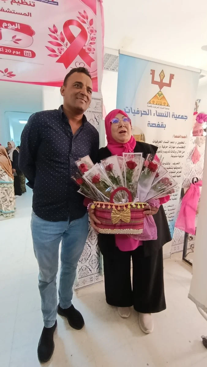 مشارك ومشاركة يحملان سلة ورود أمام لافتة جمعية النساء الحرفيات بقفصة
