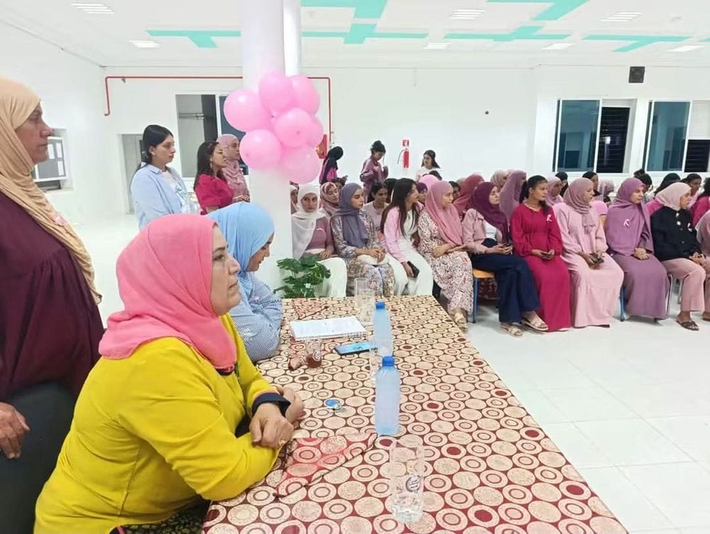 عشرات الطالبات بملابس وردية يتابعن جلسة تحسيسية في قاعة جامعية مزيّنة ببالونات وردية