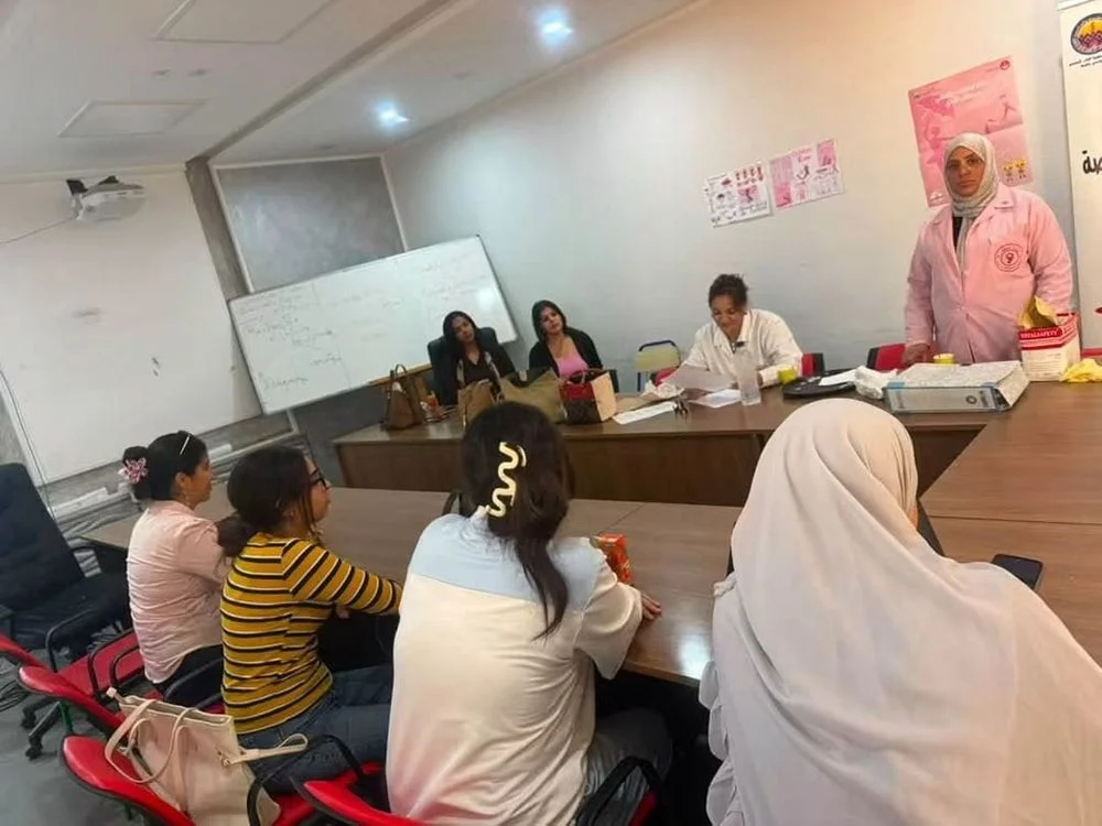 إطار صحي بمئزر وردي يقدّم حصة توعوية لطالبات جالسات حول طاولة في قاعة درس