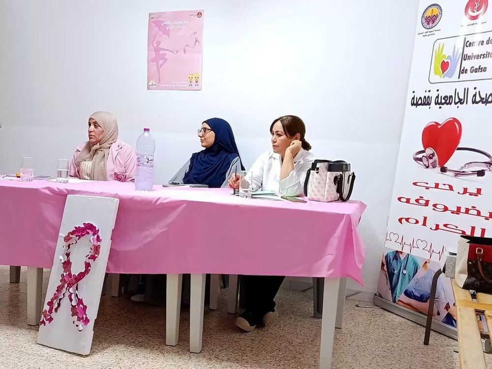 ثلاث متدخلات إلى طاولة مغطاة بالوردي، وأمامها لوحة عليها شريط وردي مصنوع من أزهار ورقية