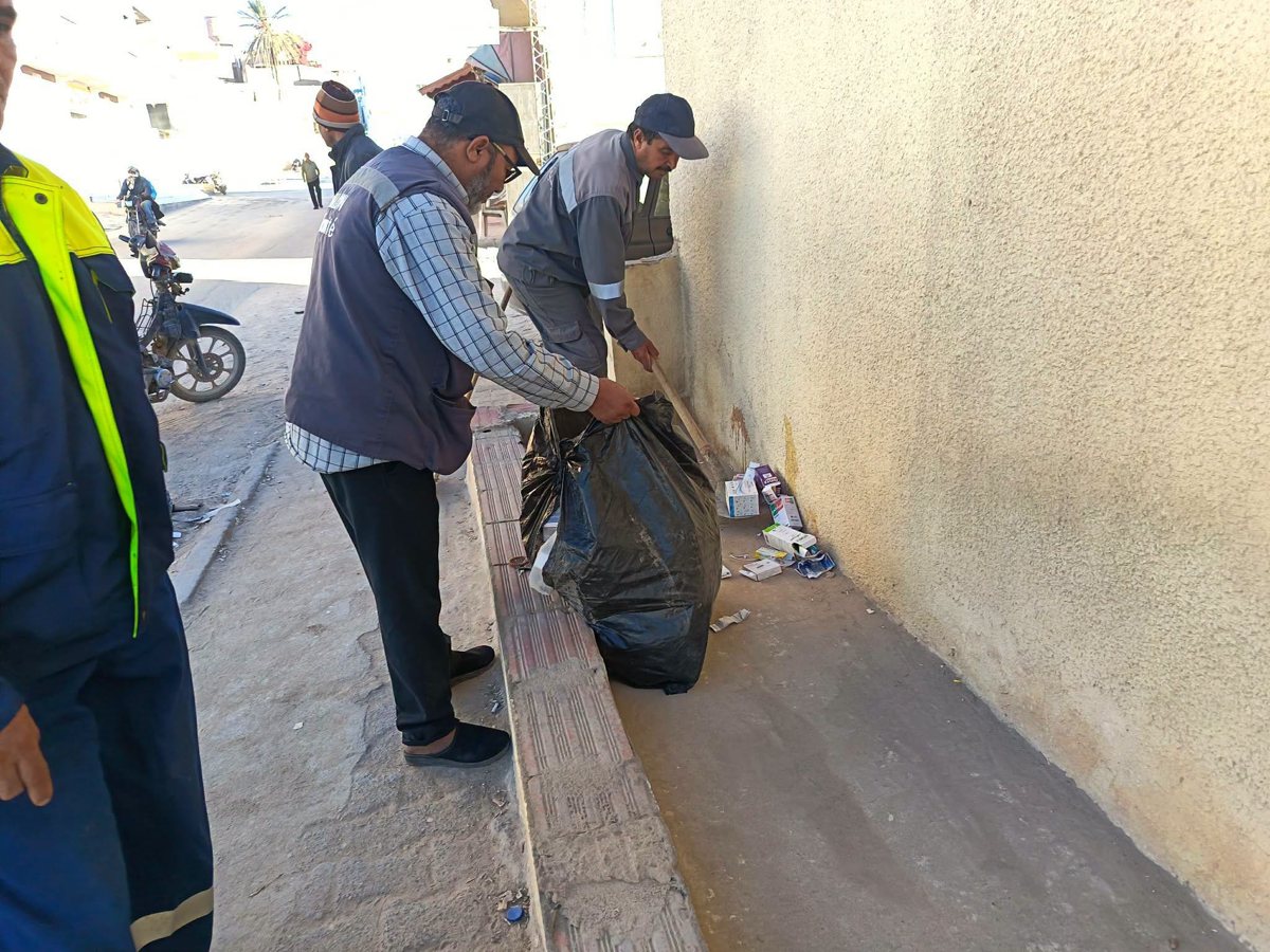 عونان يجمعان علب الأدوية والفضلات الملقاة قرب جدار في كيس أسود بأم العرائس