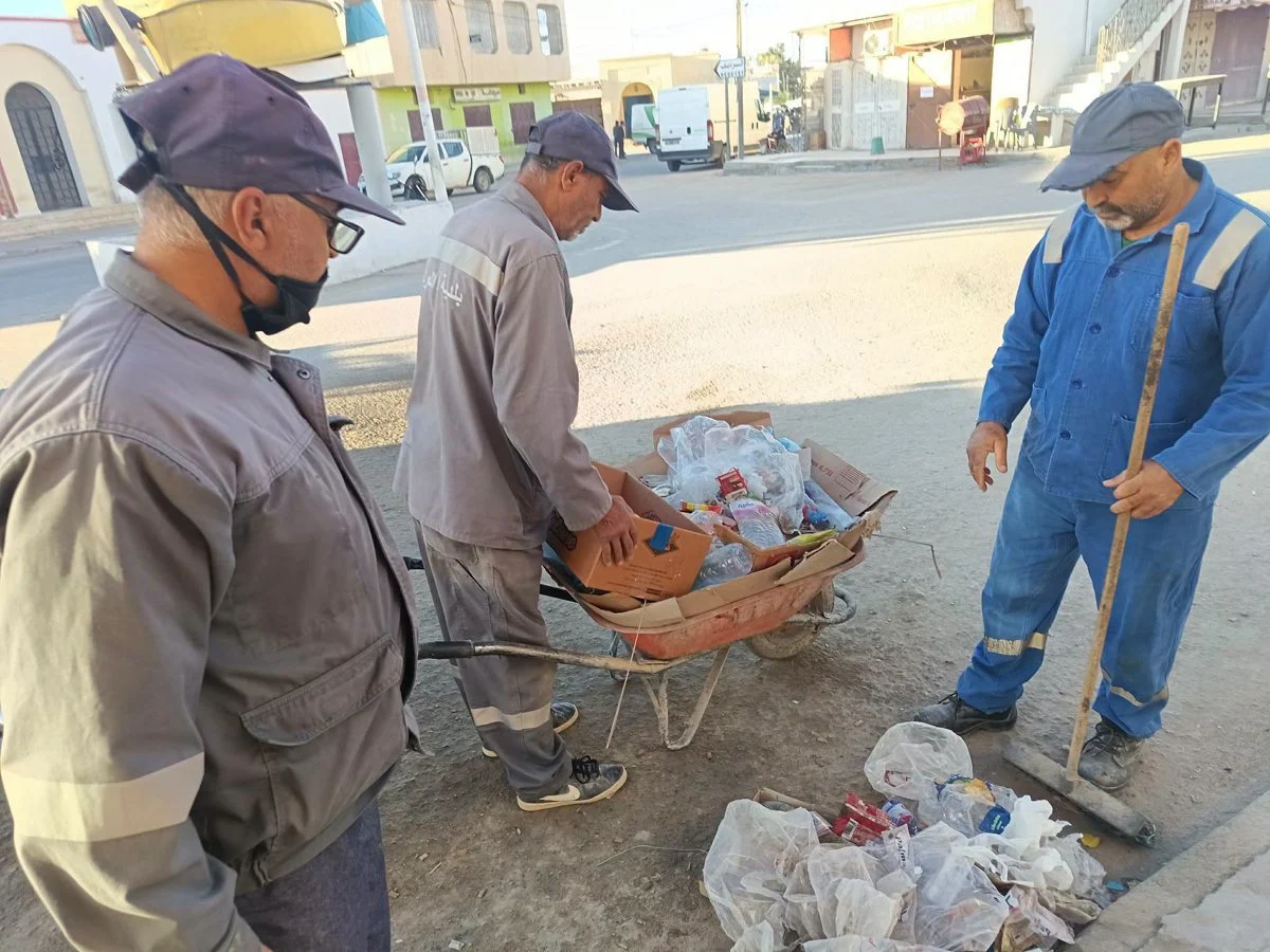ثلاثة أعوان يفرزون الكراتين والقوارير البلاستيكية في عربة يدوية بأحد مفترقات أم العرائس