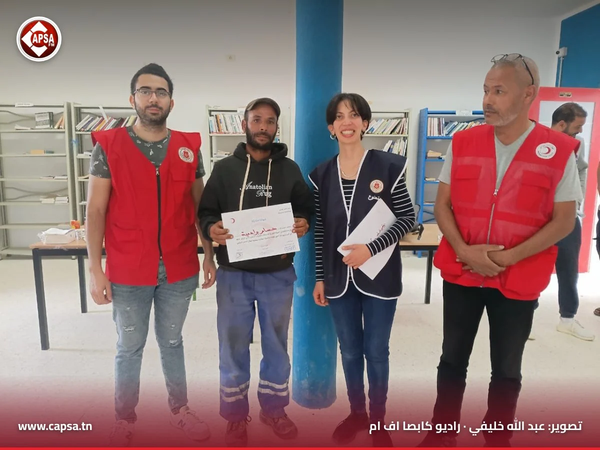 مشارك بسترة سوداء وسروال عمل أزرق يعرض شهادة المشاركة بين مؤطّري الهلال الأحمر