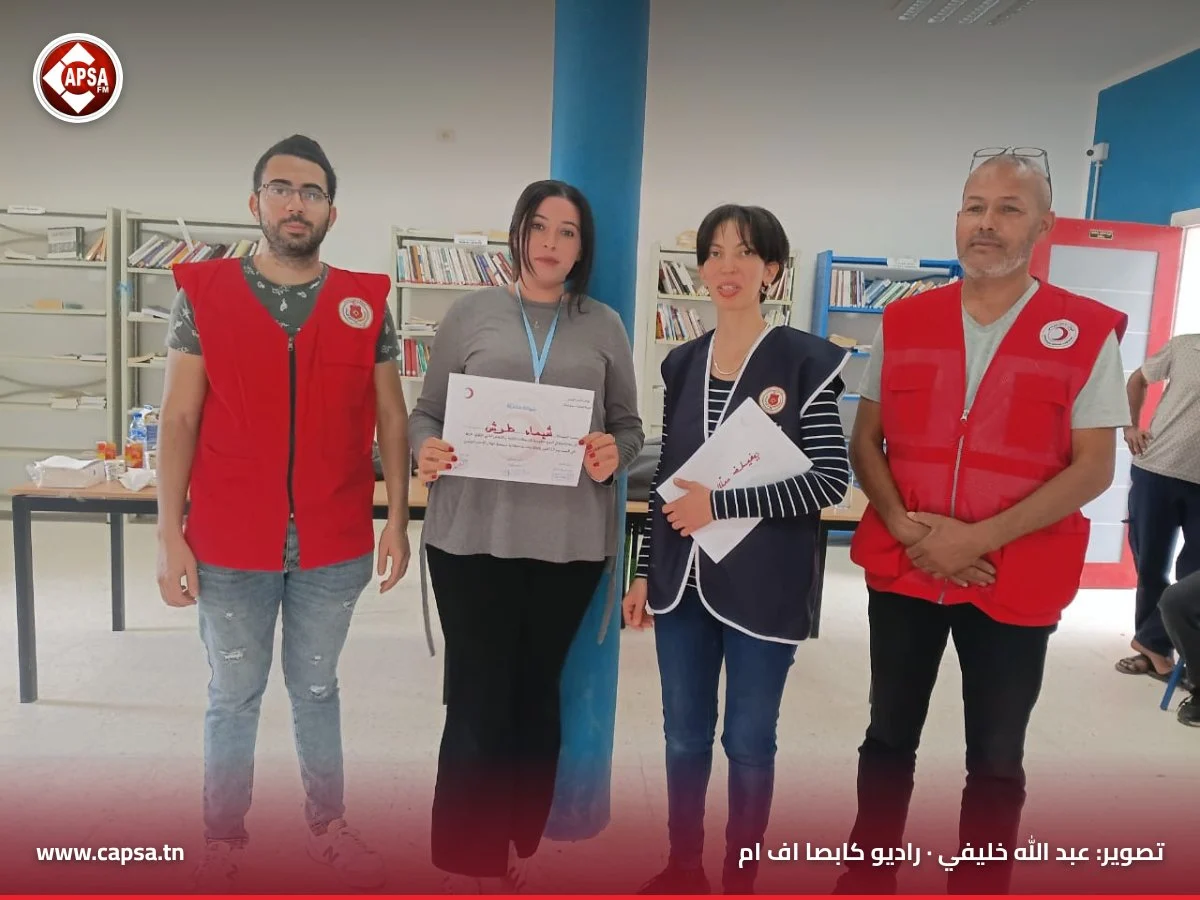 مشاركة بقميص رمادي تحمل شهادة المشاركة في الدورة التكوينية بين أعضاء الهلال الأحمر