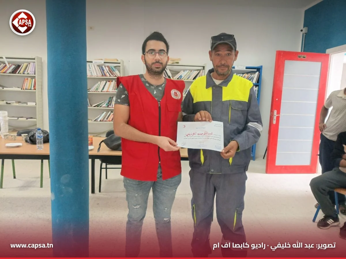 متطوع من الهلال الأحمر يسلّم شهادة المشاركة لعامل يرتدي بدلة عمل رمادية وصفراء