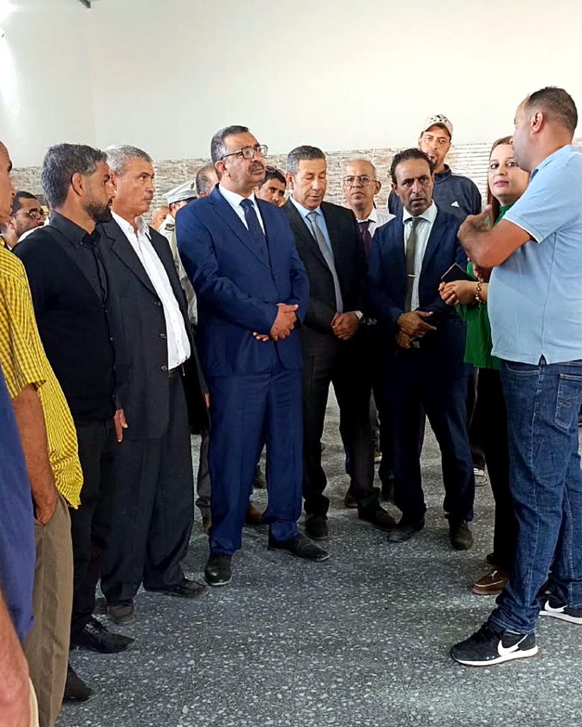 مسؤولون يستمعون إلى شرح أحد الحاضرين داخل قاعة ذات سقف معدني بسيدي بوبكر