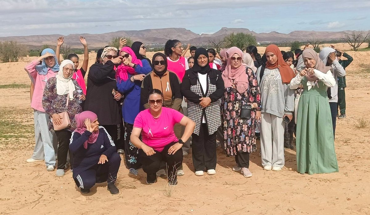 صورة جماعية لمشاركات في ماراطون المشي بالسند يحملن الشريط الوردي والجبال في الأفق