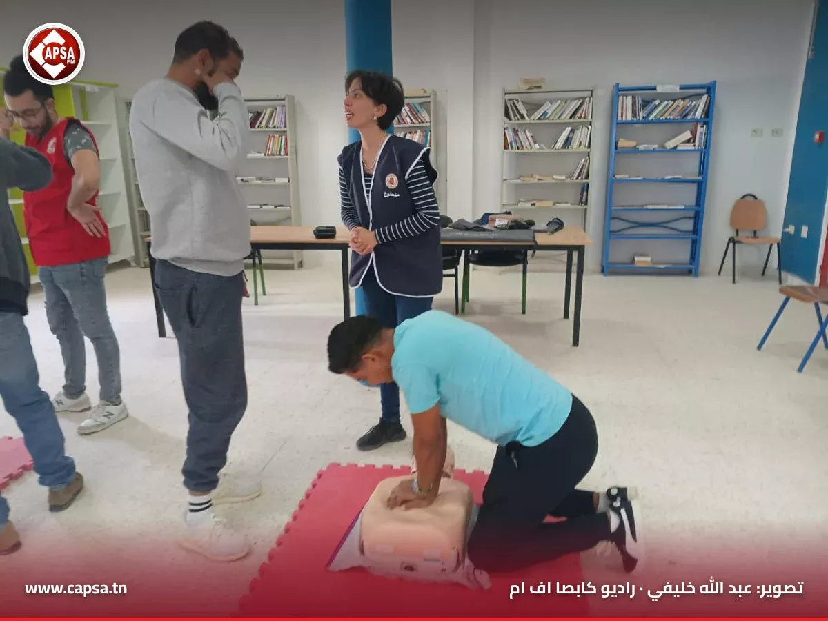 شاب بقميص أزرق يطبّق الضغطات الصدرية على دمية الإنعاش بينما تتابع متطوعة شرحها لمشارك آخر في القاعة