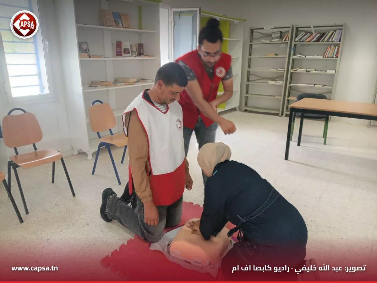 مشاركة تتدرّب على الضغطات الصدرية على دمية الإنعاش أمام متطوع من الهلال الأحمر ومتدرّب جاثٍ إلى جانبها