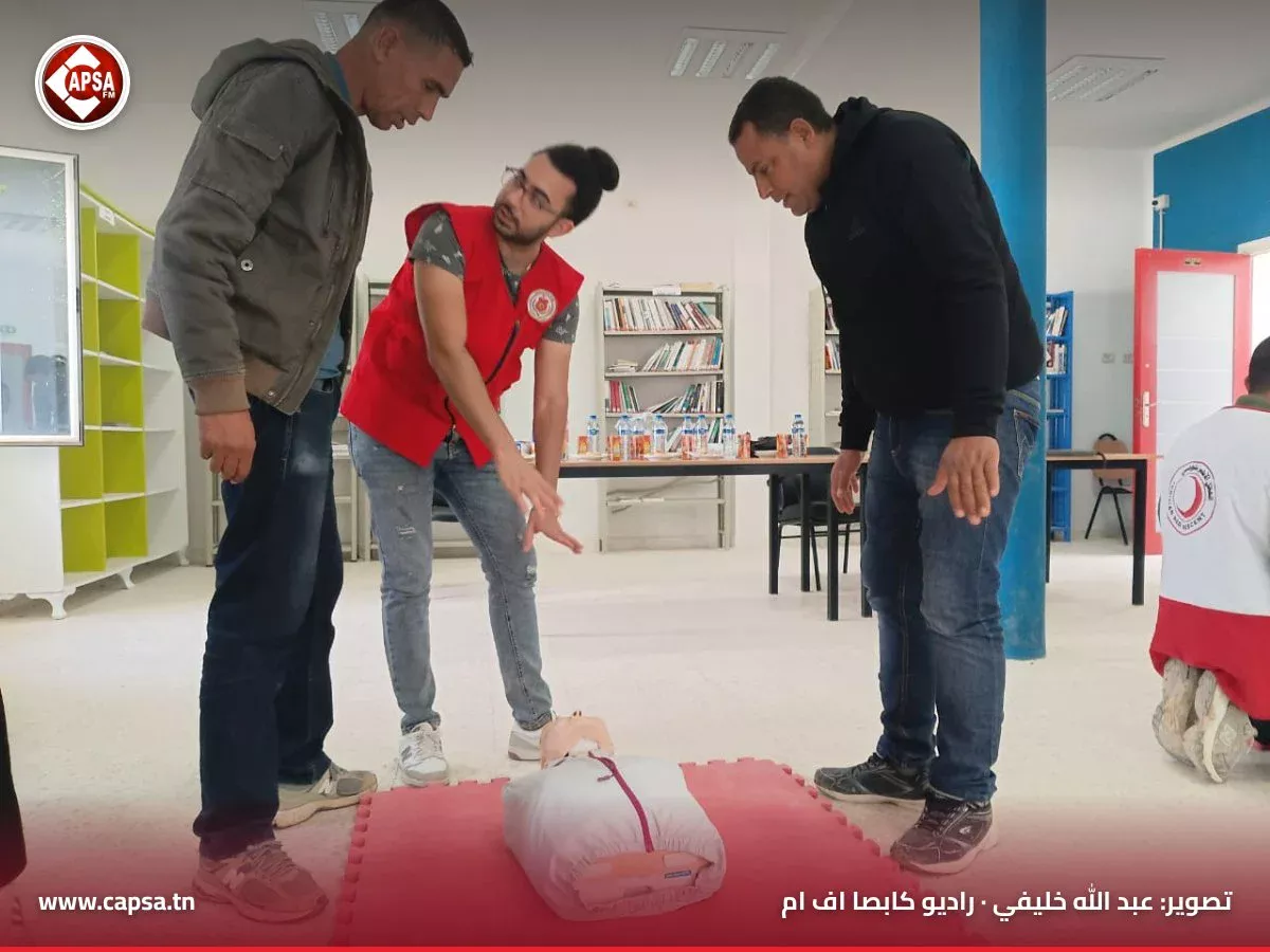 متطوع من الهلال الأحمر التونسي يشرح لمشاركَين خطوات التدخل أمام دمية تدريب ممدّدة على بساط أحمر